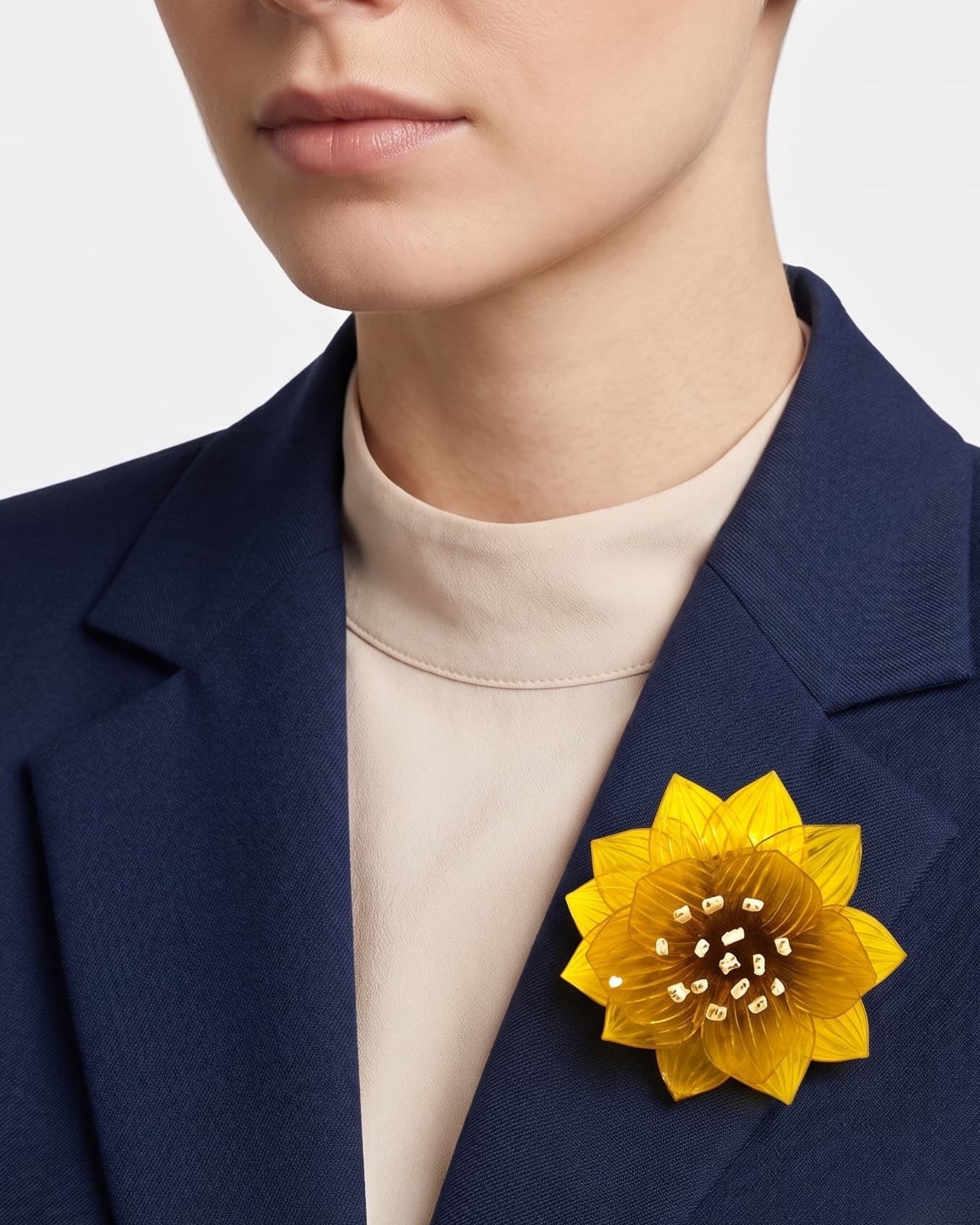 modelo de frente portando el broche maxi de loto amarillo prendido en la solapa de una blazer de sastre azul marino, destacando su escala sofisticada y su gran luminosidad.