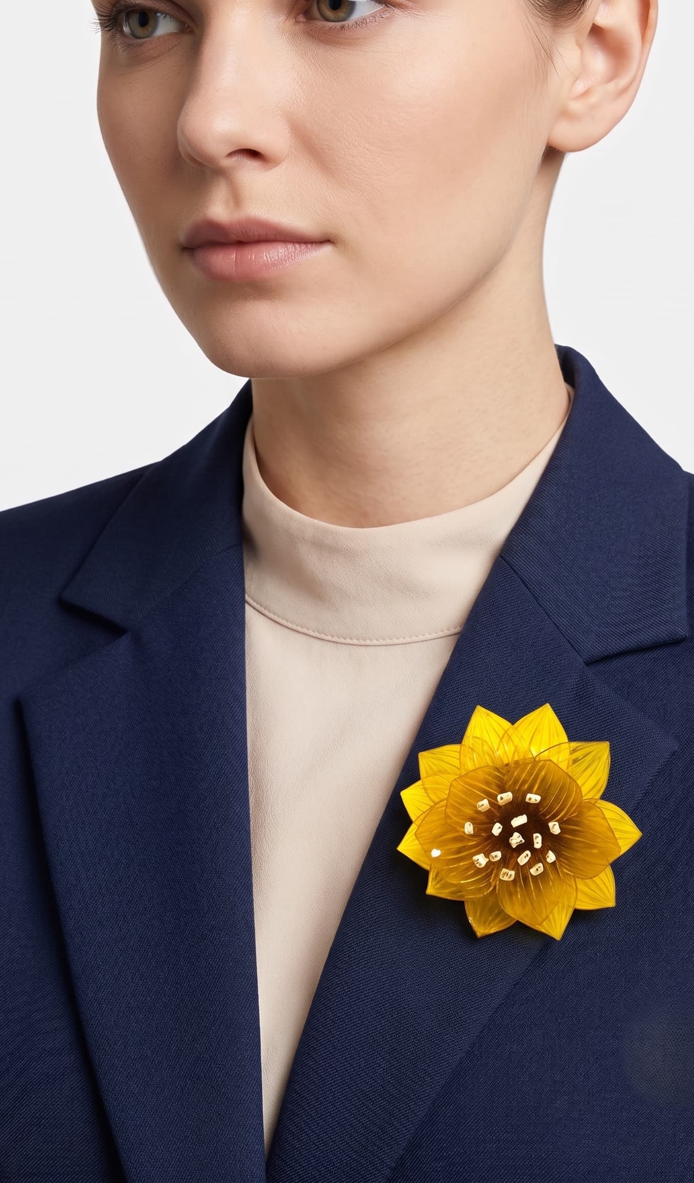 modelo de frente portando el broche maxi de loto amarillo prendido en la solapa de una blazer de sastre azul marino, destacando su escala sofisticada y su gran luminosidad.