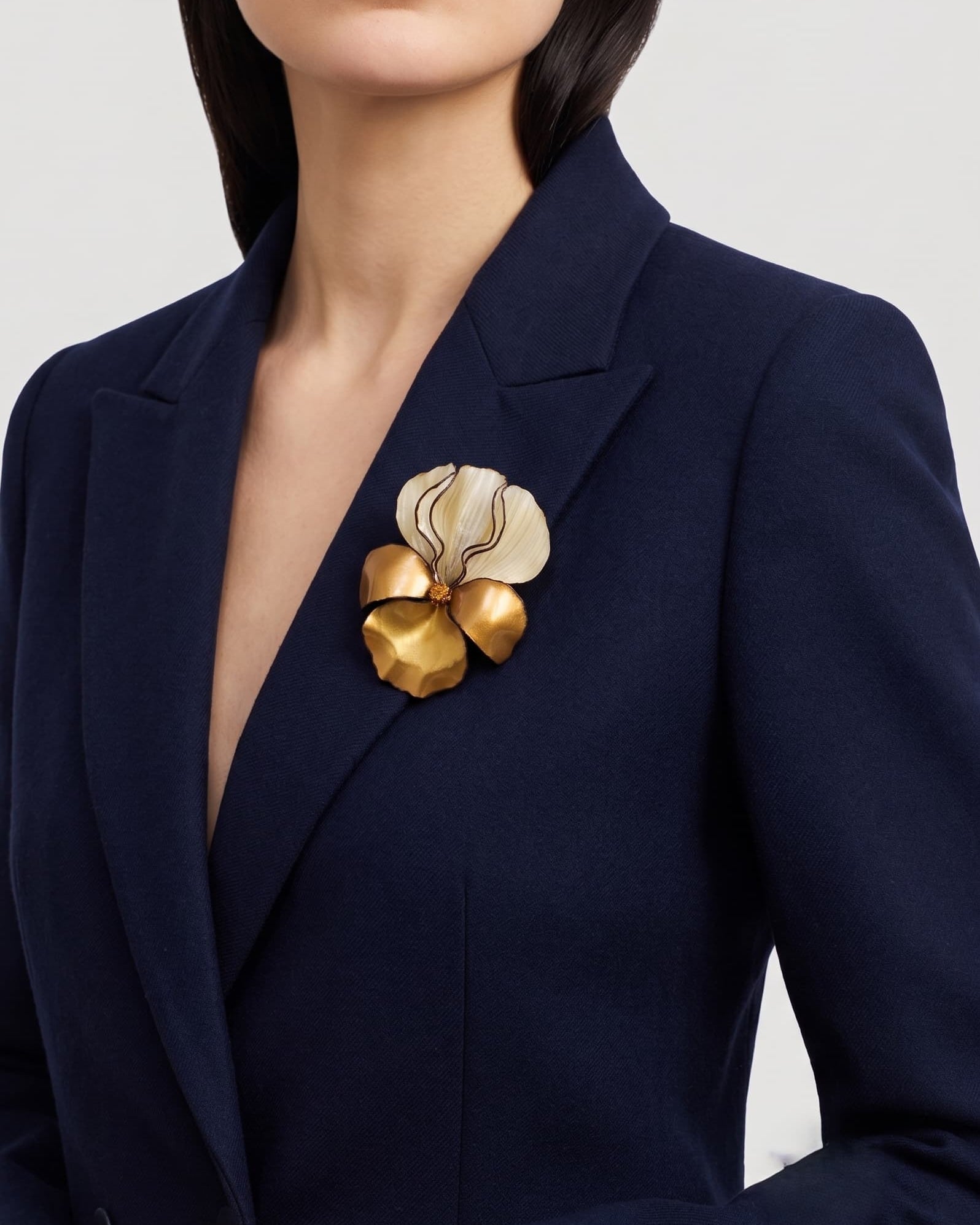 modelo luciendo el broche grande de iris dorado prendido en la solapa de una americana azul marino, mostrando su escala maximalista y elegante.