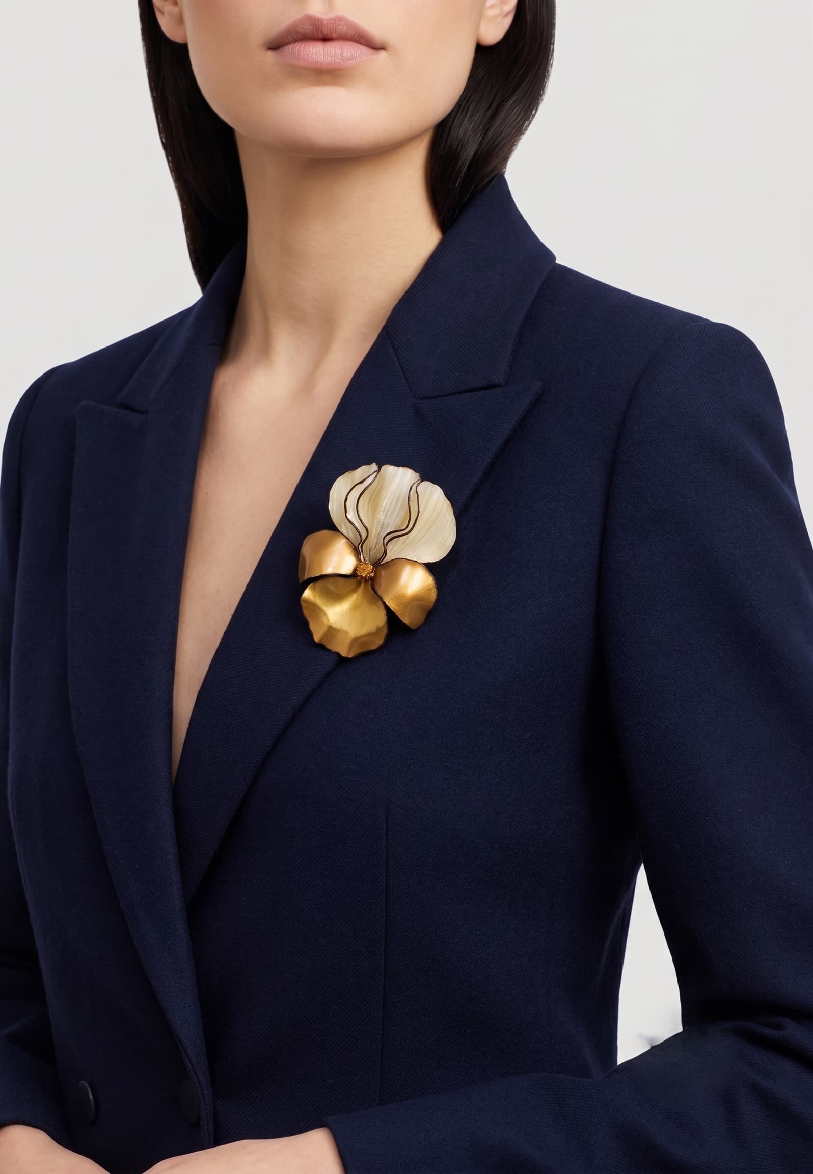 modelo luciendo el broche grande de iris dorado prendido en la solapa de una americana azul marino, mostrando su escala maximalista y elegante.