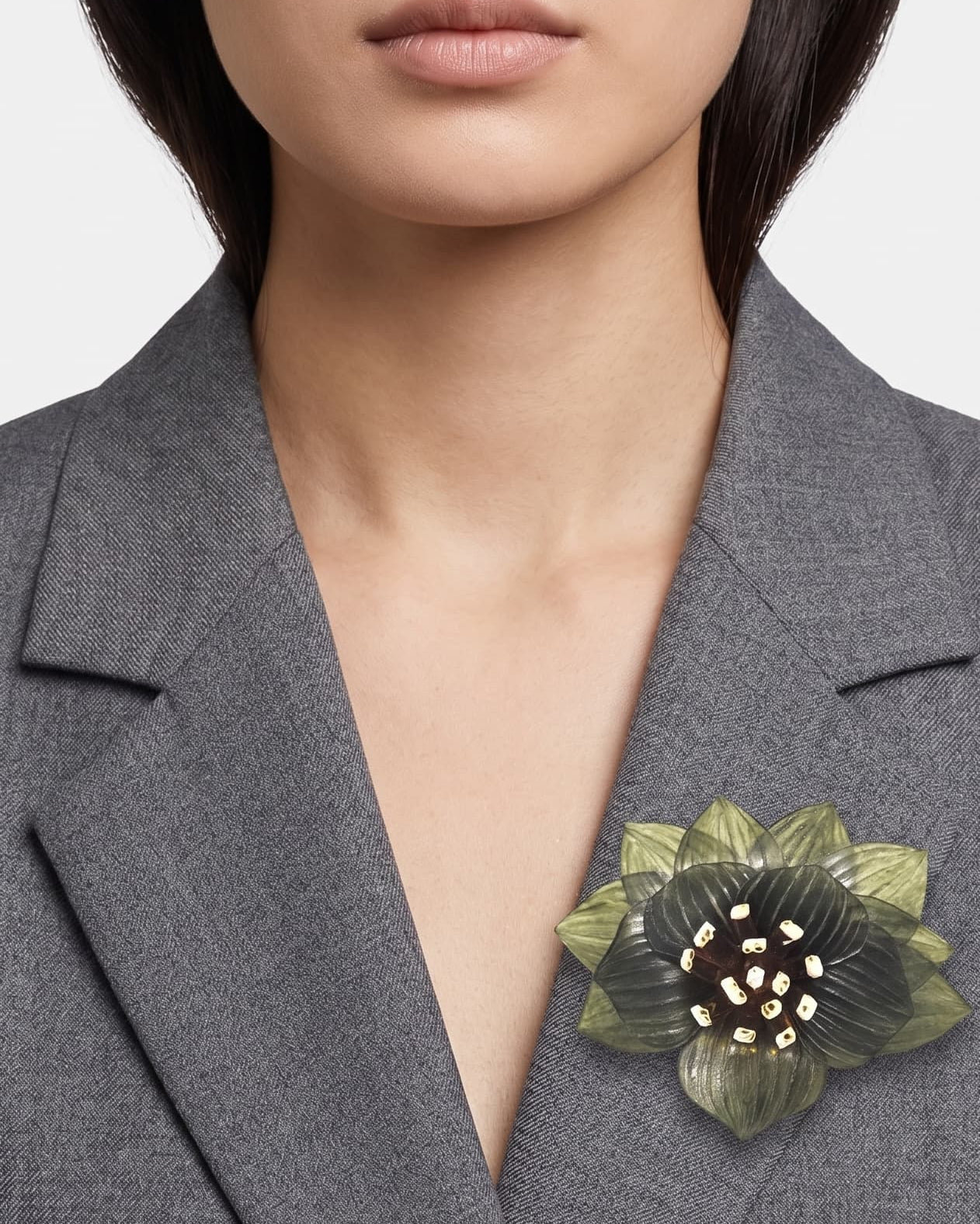 modelo luciendo el broche maxi de loto verde prendido en la solapa de una blazer gris de sastre, mostrando su escala sofisticada y elegante.