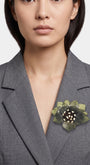modelo luciendo el broche maxi de loto verde prendido en la solapa de una blazer gris de sastre, mostrando su escala sofisticada y elegante.