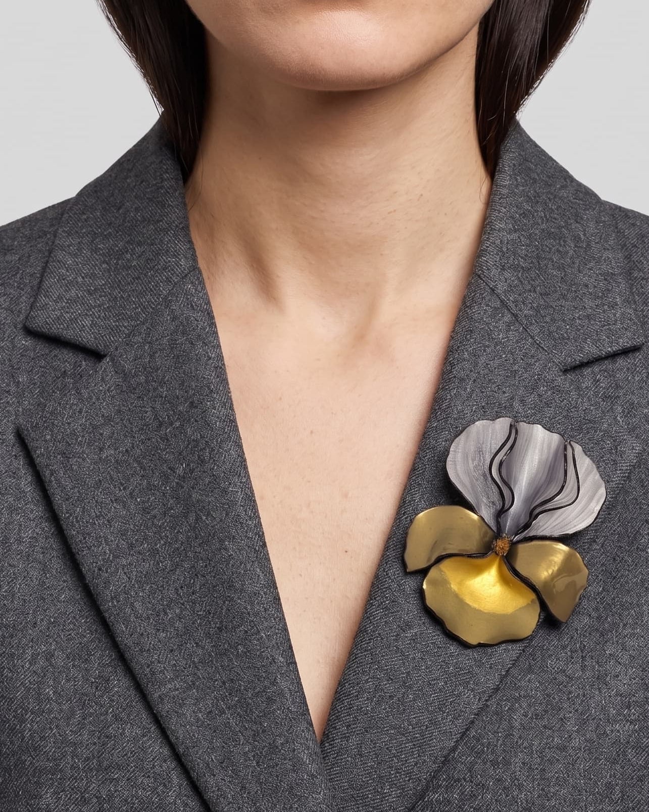 modelo luciendo el broche maxi de iris plata y oro prendido en la solapa de una blazer de sastre gris, apreciando su escala y sofisticación.