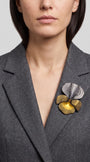 modelo luciendo el broche maxi de iris plata y oro prendido en la solapa de una blazer de sastre gris, apreciando su escala y sofisticación.