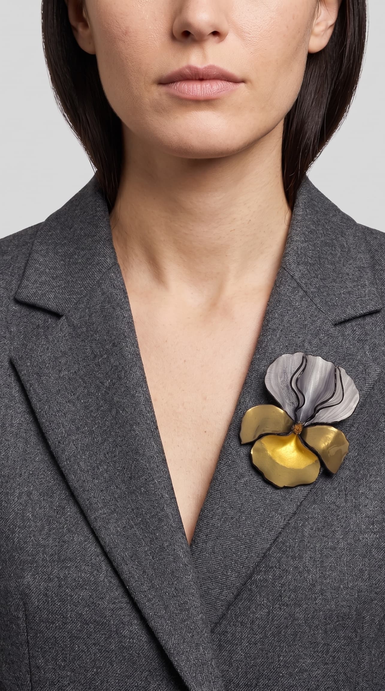 modelo luciendo el broche maxi de iris plata y oro prendido en la solapa de una blazer de sastre gris, apreciando su escala y sofisticación.