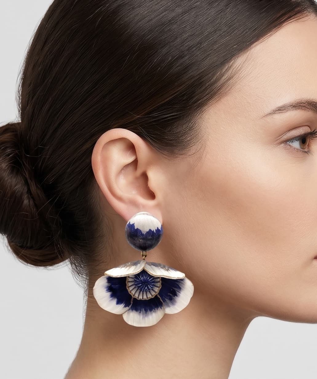 modelo luciendo el pendiente colgante de flor azul y blanca, apreciando su escala maximalista, su relieve tridimensional y cómo adorna el rostro con sofisticación.