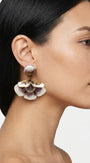 modelo luciendo el pendiente colgante de flor malva y blanca, apreciando su escala maximalista, su relieve tridimensional y cómo adorna el rostro con sofisticación.