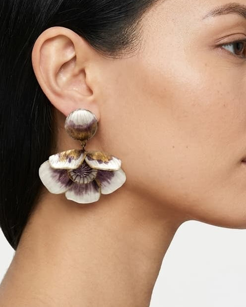 modelo luciendo el pendiente colgante de flor malva y blanca, apreciando su escala maximalista, su relieve tridimensional y cómo adorna el rostro con sofisticación.