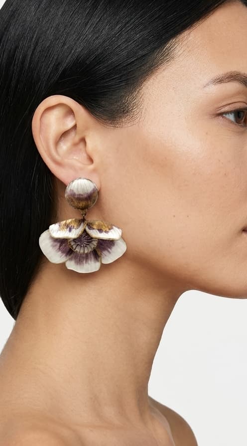 modelo luciendo el pendiente colgante de flor malva y blanca, apreciando su escala maximalista, su relieve tridimensional y cómo adorna el rostro con sofisticación.