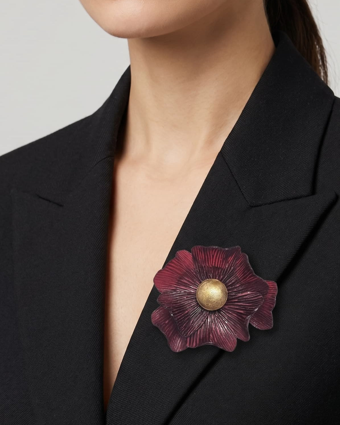 modelo vistiendo una blazer de sastre negra con el broche de anémona grande burdeos prendido en la solapa, destacando su escala sofisticada.