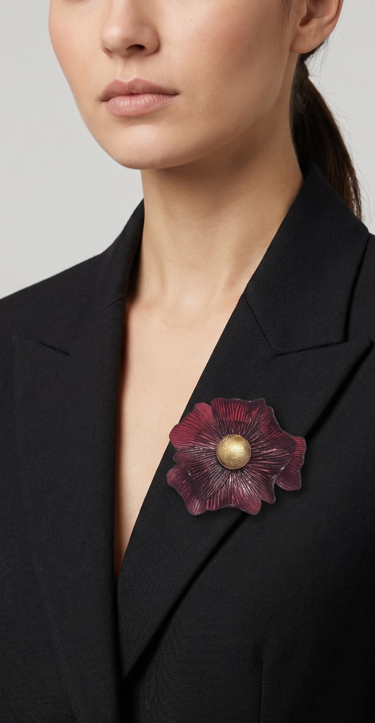 modelo vistiendo una blazer de sastre negra con el broche de anémona grande burdeos prendido en la solapa, destacando su escala sofisticada.