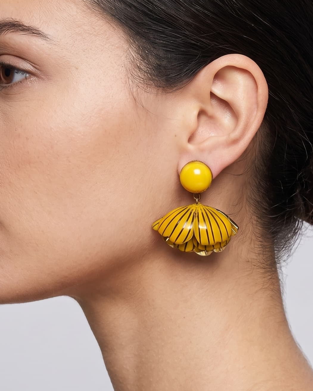 vista de perfil del pendiente amarillo de Ciléa Paris colocado en una modelo, detallando el ajuste de su cierre de pinza y su elegante escala tridimensional.