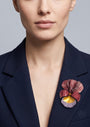 modelo luciendo el broche maxi de iris burdeos prendido en la solapa de una americana de sastre azul marino, apreciando su escala maximalista y elegante.