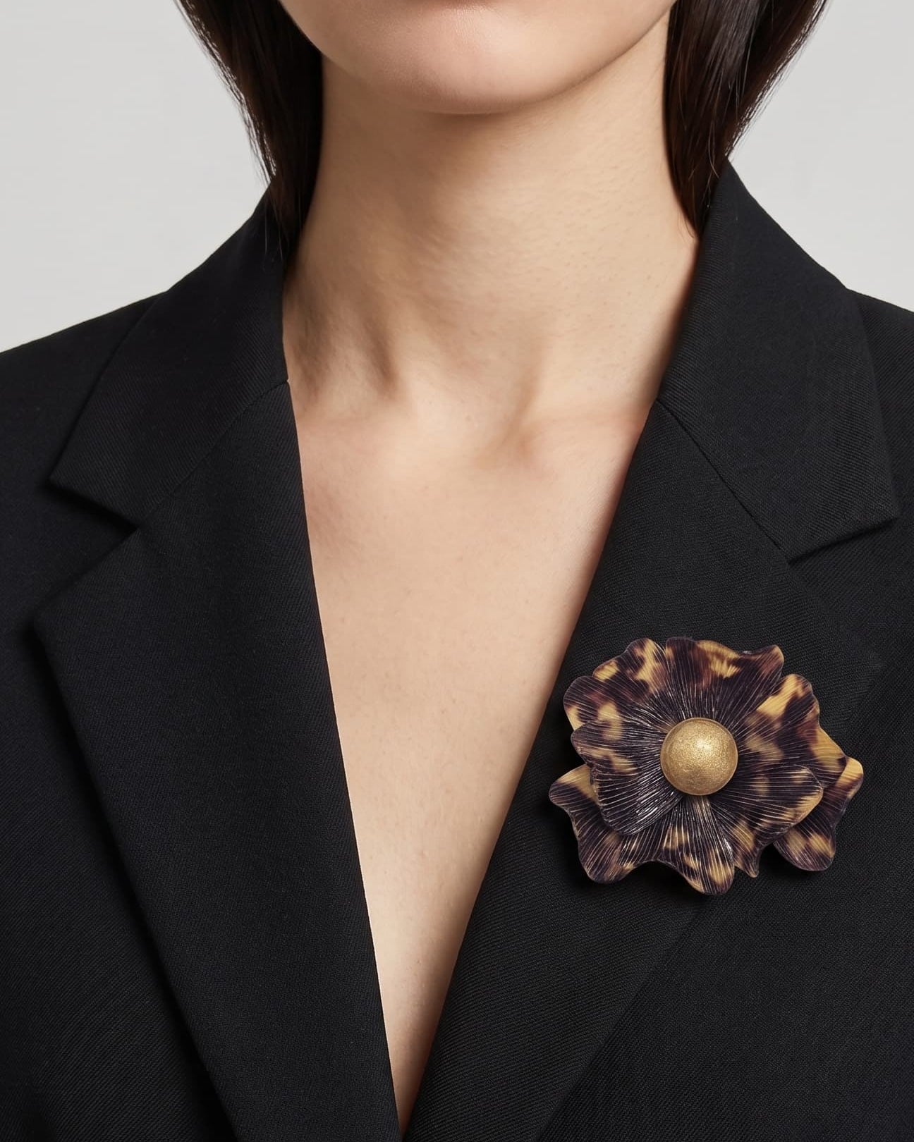 modelo luciendo el broche maxi de anémona carey prendido en la solapa de una americana de sastre negra, mostrando su escala y sofisticación.