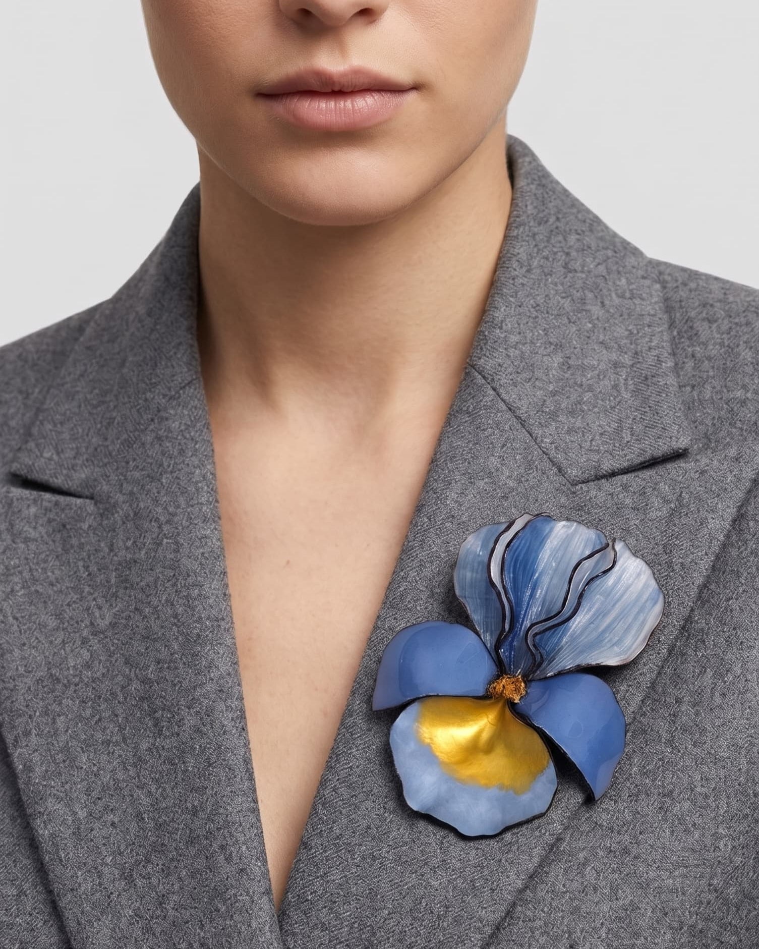modelo luciendo el broche maxi de iris azul prendido en la solapa de una americana de sastre gris claro, apreciando su escala maximalista y elegante.