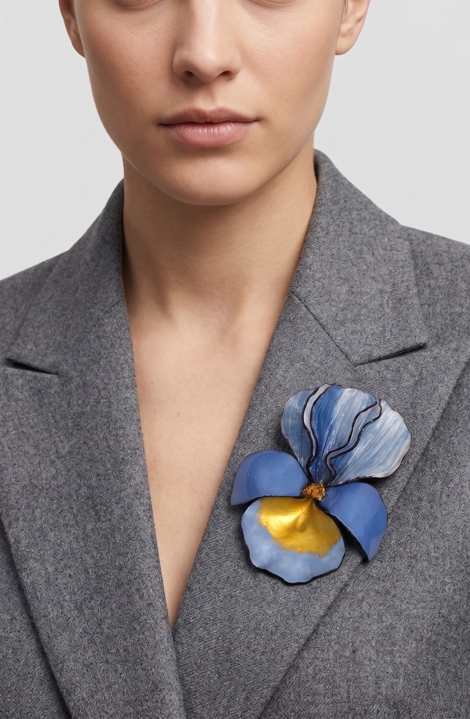 modelo luciendo el broche maxi de iris azul prendido en la solapa de una americana de sastre gris claro, apreciando su escala maximalista y elegante.