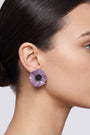 modelo luciendo el pendiente de botón de amapola violeta, apreciando su escala delicada y cómo se acopla con elegancia al lóbulo aportando un matiz de color sofisticado.