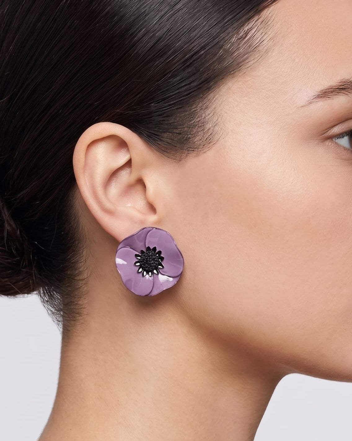 modelo luciendo el pendiente de botón de amapola violeta, apreciando su escala delicada y cómo se acopla con elegancia al lóbulo aportando un matiz de color sofisticado.