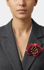modelo de frente luciendo el broche maxi de loto rojo prendido en la solapa de una americana de sastre gris oscuro, mostrando su escala sofisticada y elegante.