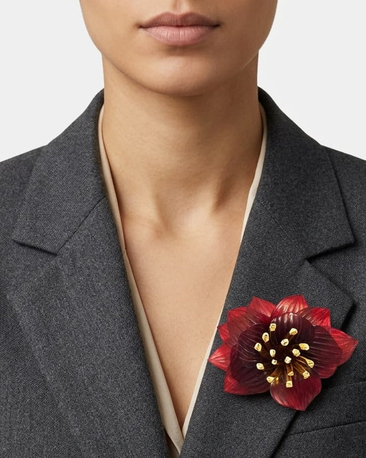modelo de frente luciendo el broche maxi de loto rojo prendido en la solapa de una americana de sastre gris oscuro, mostrando su escala sofisticada y elegante.