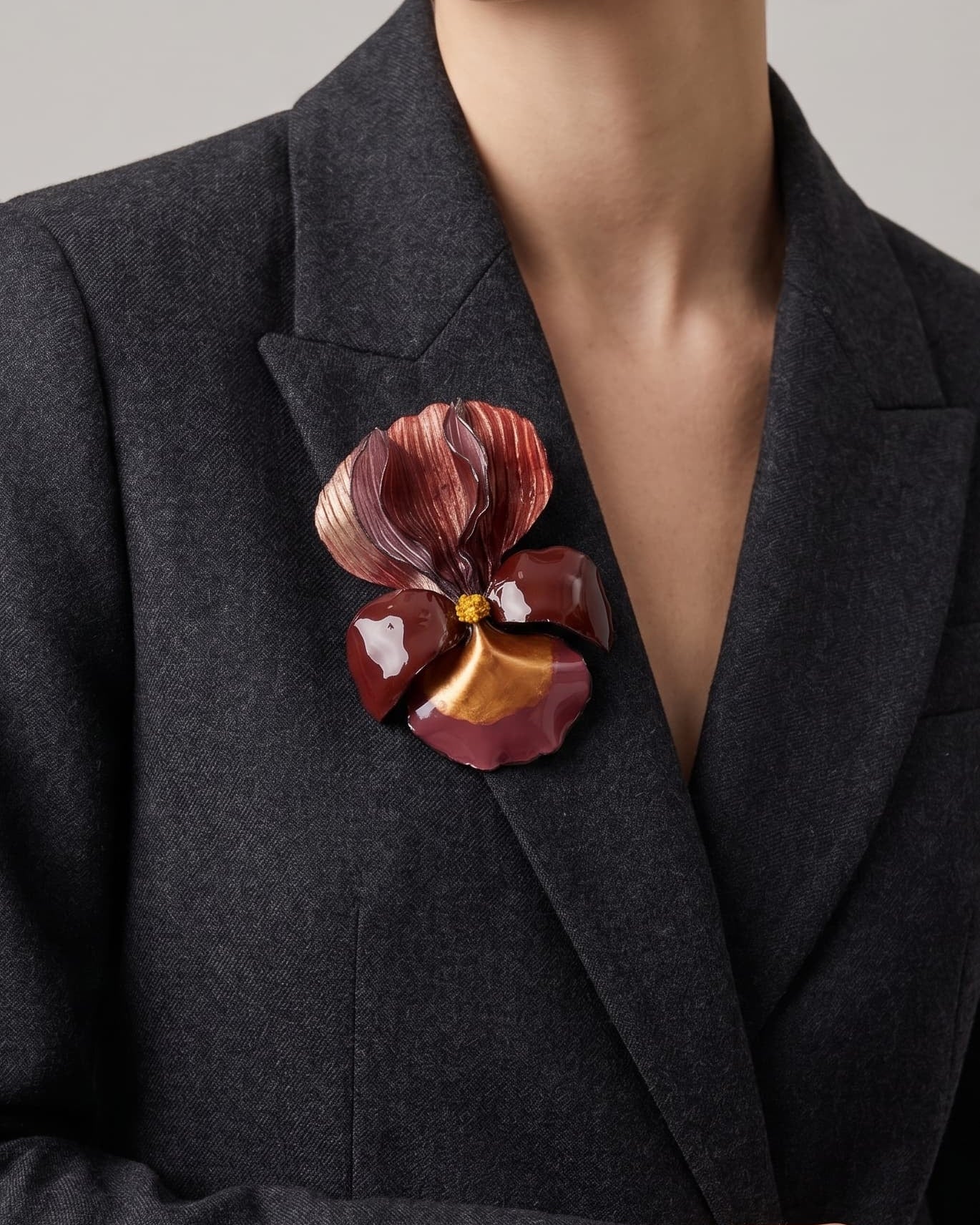 modelo luciendo el broche maxi de iris rojo prendido en la solapa de una americana de sastre gris oscuro, apreciando su escala maximalista y elegante.