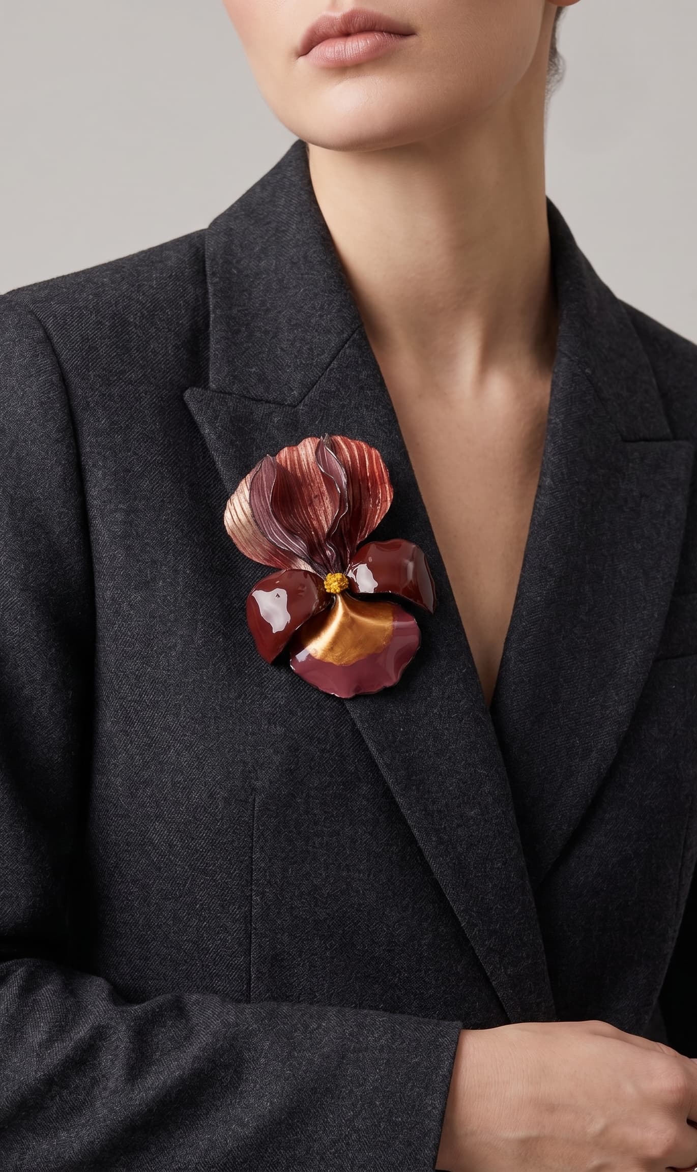 modelo luciendo el broche maxi de iris rojo prendido en la solapa de una americana de sastre gris oscuro, apreciando su escala maximalista y elegante.