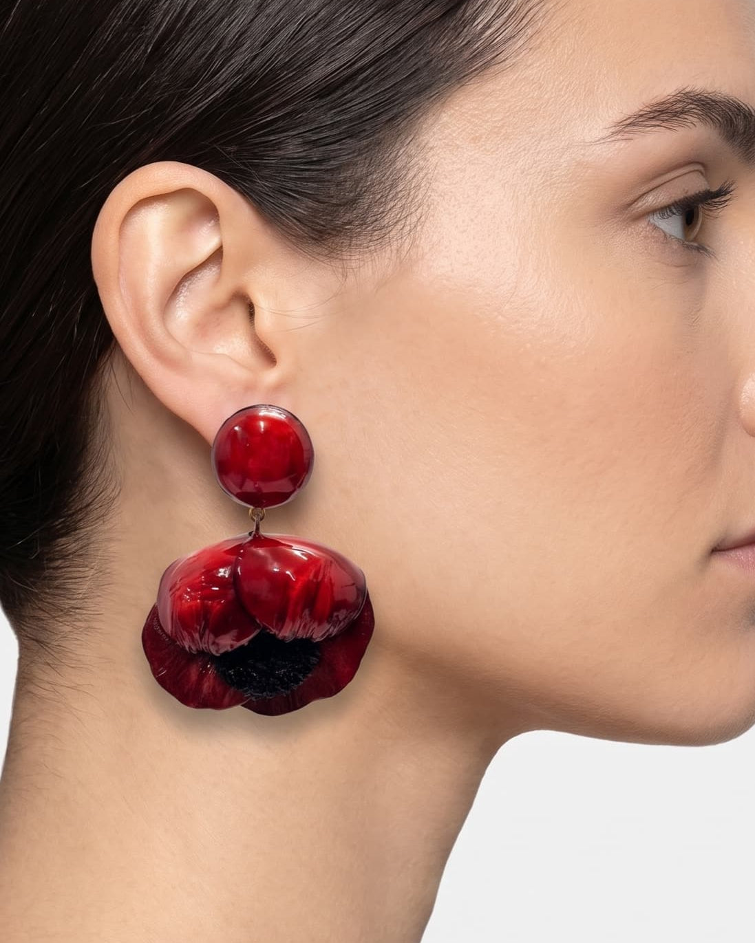 modelo luciendo el pendiente colgante de amapola roja, apreciando su escala maximalista, su relieve tridimensional y cómo adorna el rostro con sofisticación.