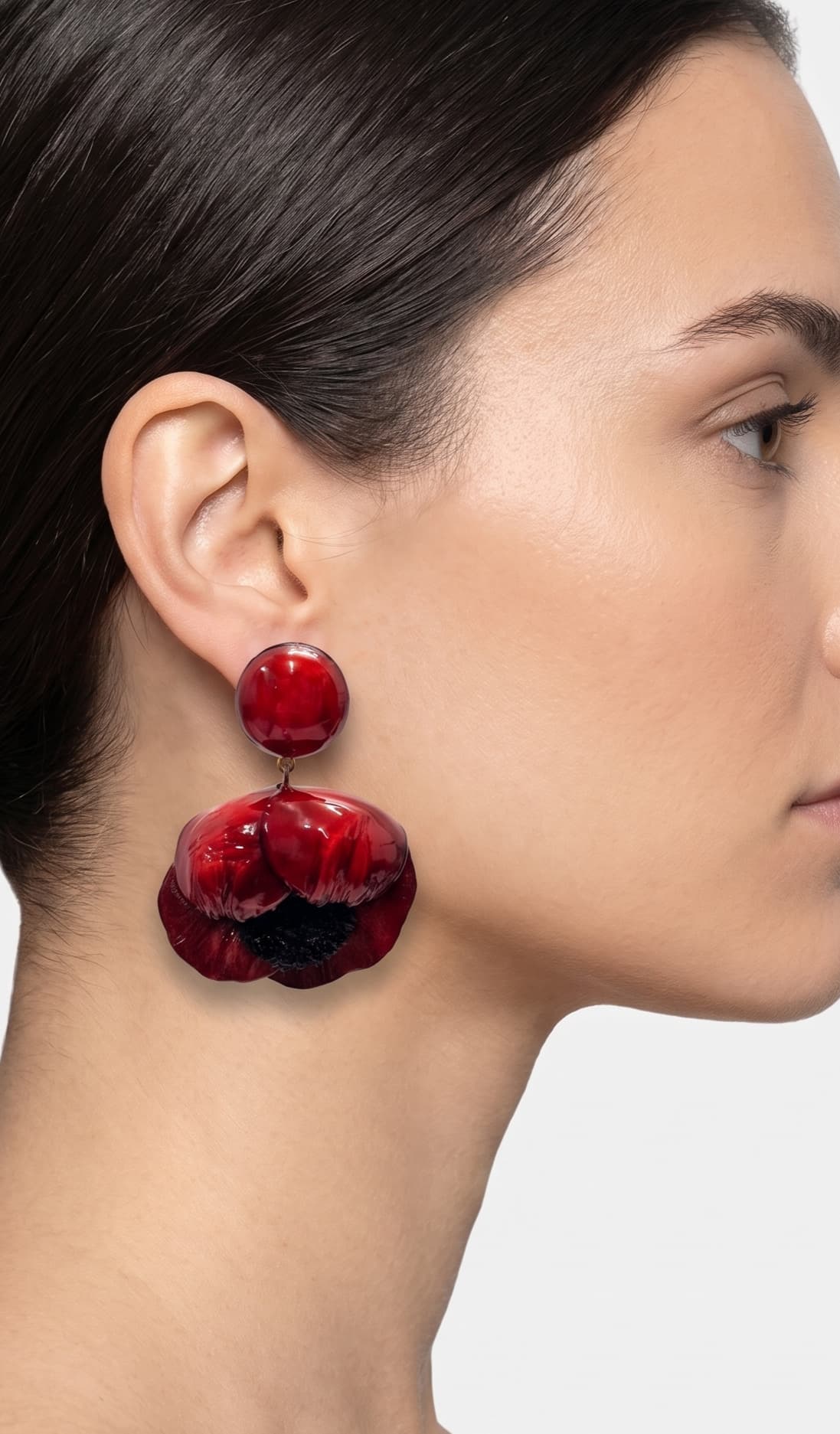 modelo luciendo el pendiente colgante de amapola roja, apreciando su escala maximalista, su relieve tridimensional y cómo adorna el rostro con sofisticación.