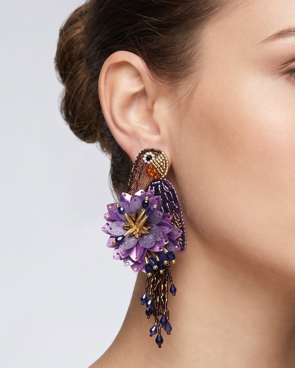 modelo luciendo el pendiente Perroquet Violet en la oreja, apreciando su silueta de ave, volumen floral y escala sobre la piel.