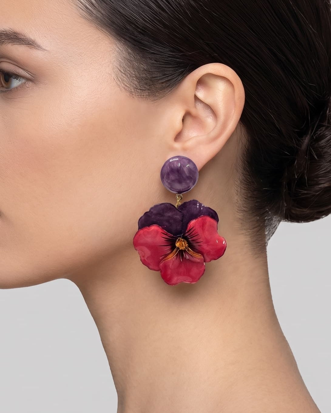 vista de perfil del pendiente de pensamiento violeta y rojo de Ciléa Paris colocado en el lóbulo de una modelo, detallando su imponente caída, su escala extra grande de 7x5 cm y su textura esmaltada.