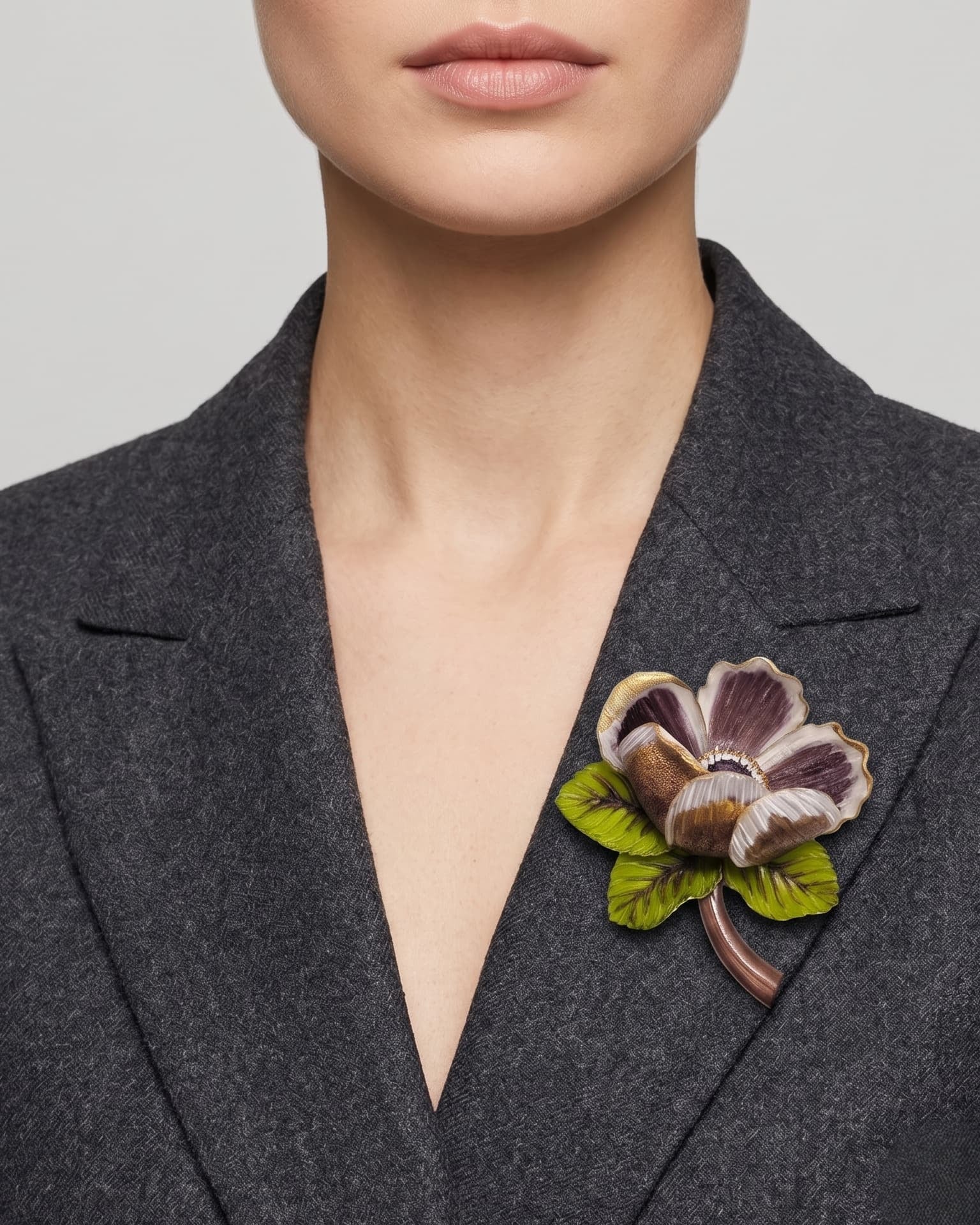modelo luciendo el broche maxi de amapola violeta prendido en la solapa de una chaqueta de sastre gris oscuro, mostrando su escala elegante y volumetría.