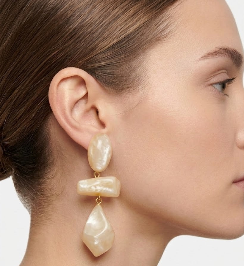 Mujer luciendo los pendientes Isma Dune de Dominique Denaive sobre un look en tonos crema, destacando su volumen y elegancia.
