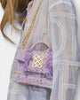 Bolso Kooreloo New Yorker Petite lila llevado al hombro con un look de blusa blanca bordada.