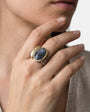 Anillo ancho de diseño con piedra azul oscura visto puesto en la mano de una modelo