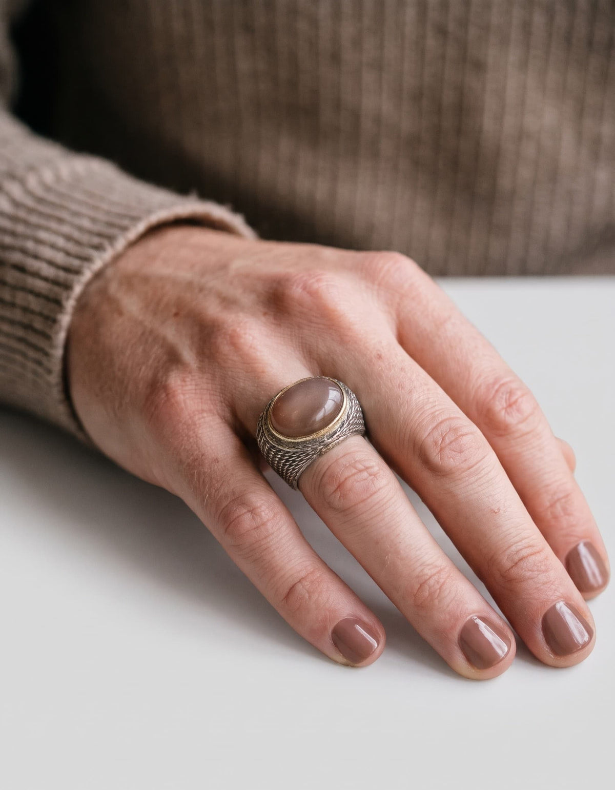 Anillo ancho de plata con cabujón ovalado marrón visto puesto en la mano de una modelo