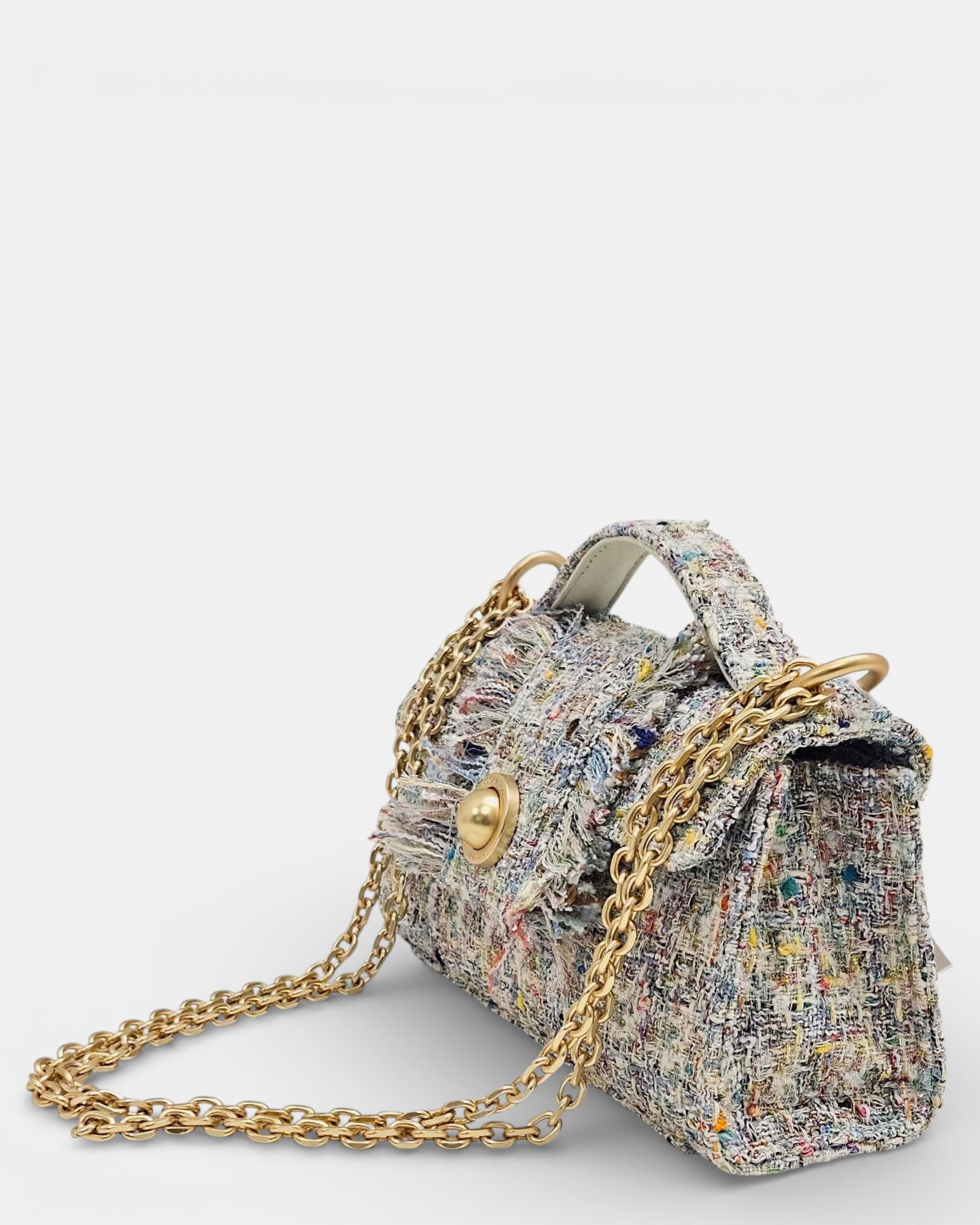 Vista lateral de bolso de tweed texturizado que muestra el asa superior, la cadena de hombro dorada y el cierre decorativo metálico.