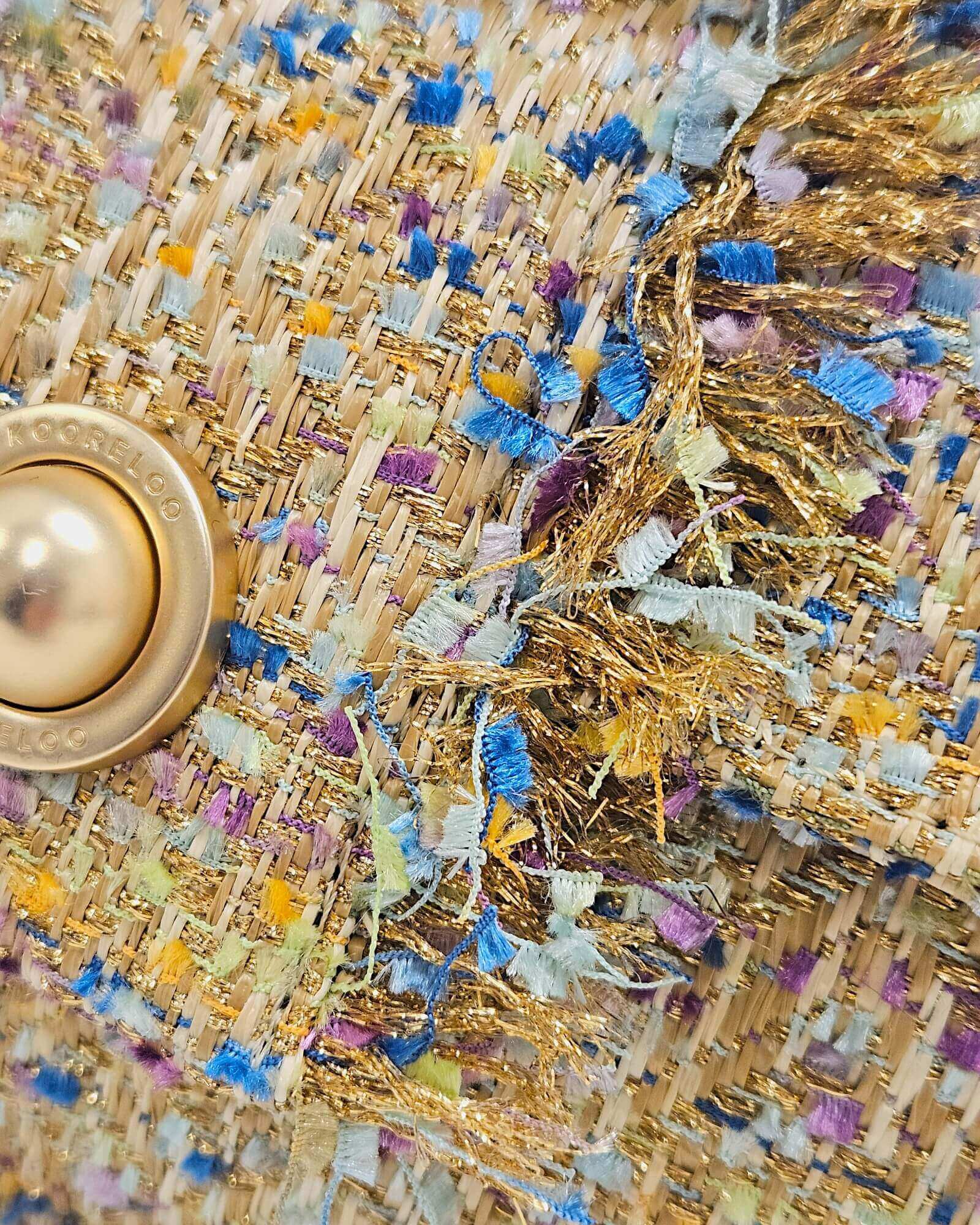 Primer plano de la textura del tejido tweed Kooreloo con hilos dorados, azules y púrpuras.