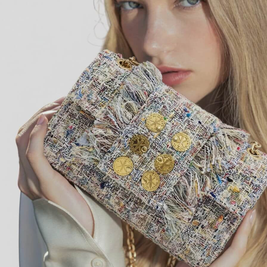 Bolso en modelo frontal de tweed en tonos beige y pastel con seis monedas doradas decorativas y laterales con flecos deshilachados.