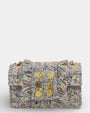 Bolso frontal de tweed en tonos beige y pastel con seis monedas doradas decorativas y laterales con flecos deshilachados.