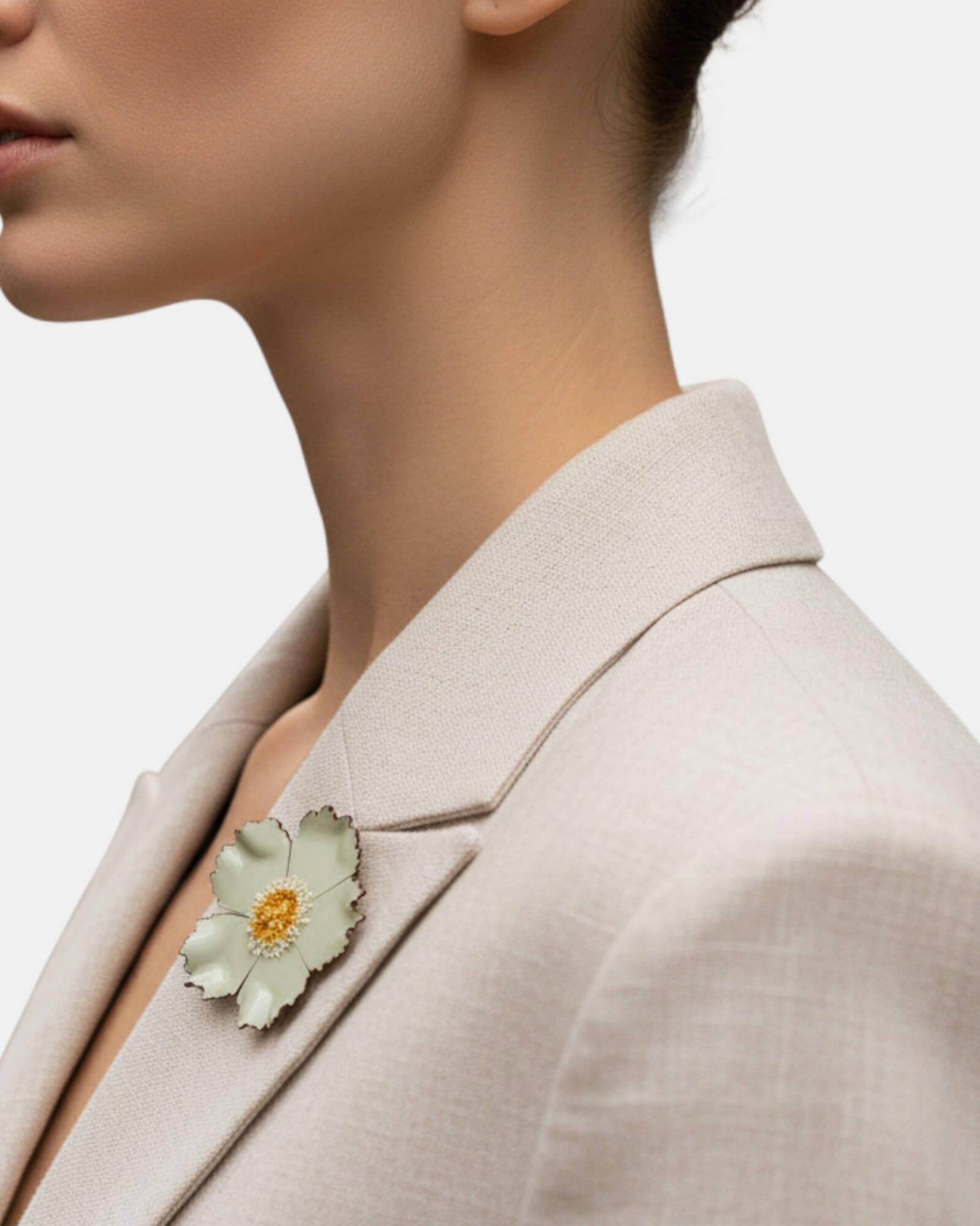 Mujer con blazer beige luciendo un broche de flor silvestre verde agua en la solapa, estilo natural y sofisticado.