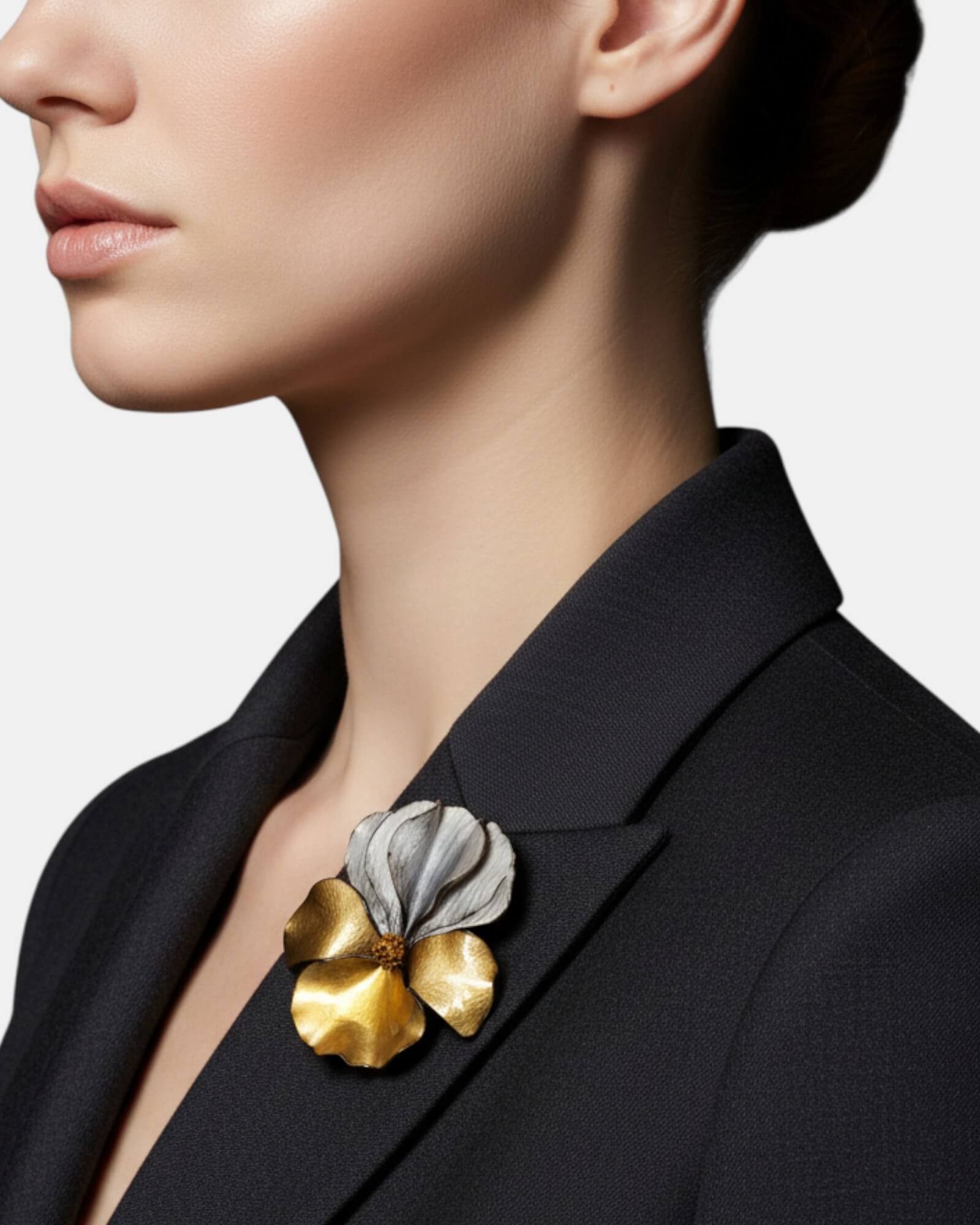 Mujer con blazer negro luciendo un broche de flor gris y oro en la solapa, estilo ejecutivo y elegante.