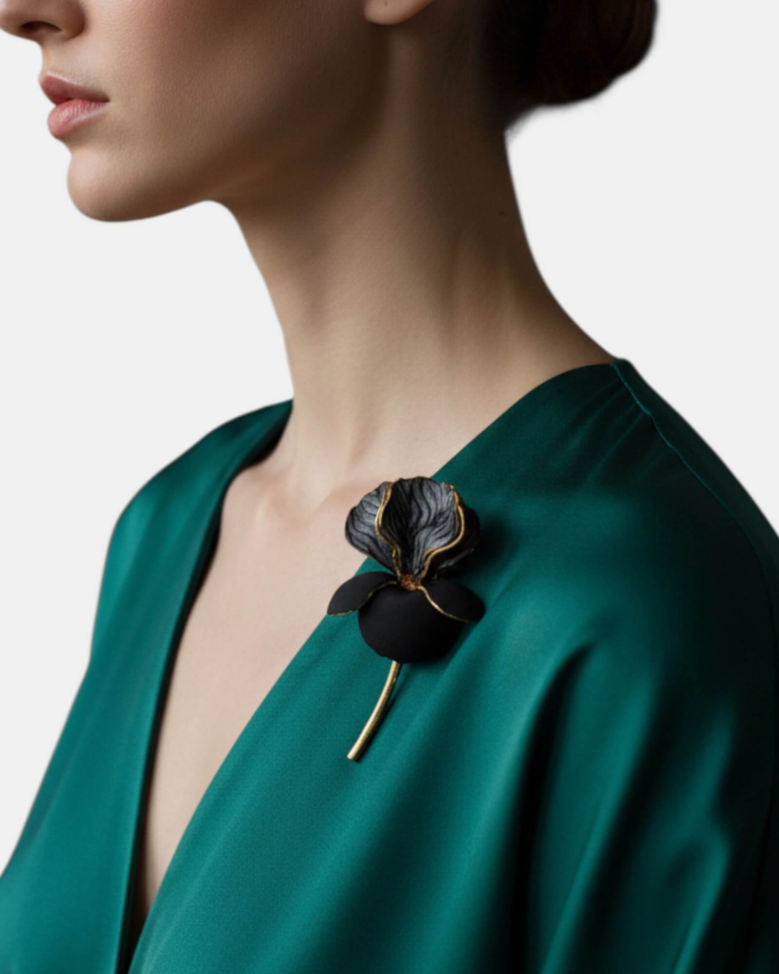 Mujer luciendo un broche de flor negra y oro sobre un vestido de seda verde esmeralda, accesorio de lujo para eventos.