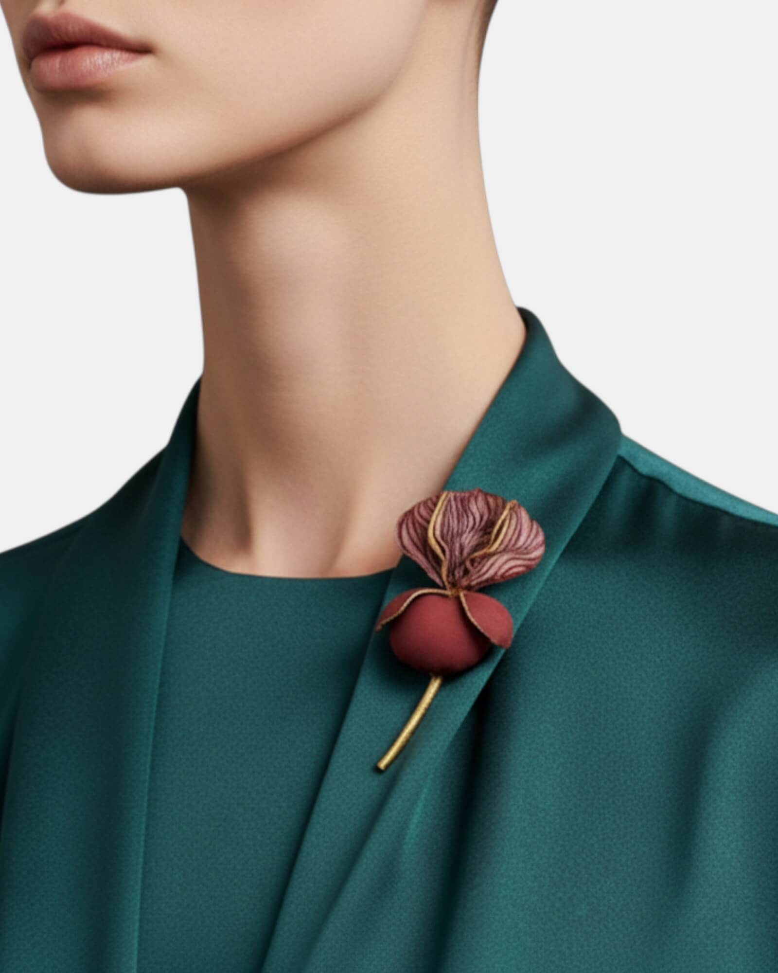 Mujer con broche artesanal de flor burdeos sobre chaqueta verde esmeralda de seda, detalle de joyería de autor.