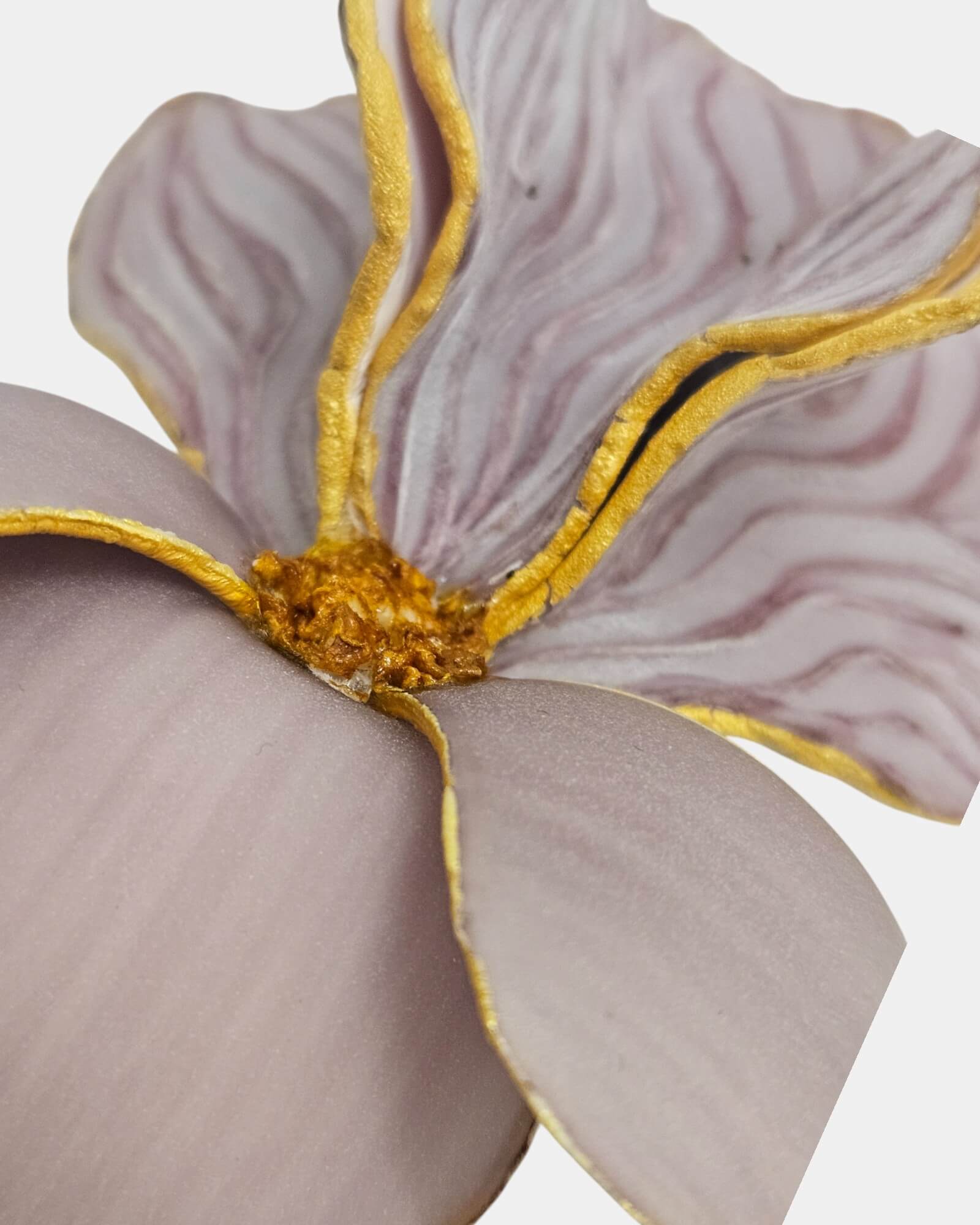 Detalle en primer plano de broche artesanal en forma de flor malva con bordes dorados y texturas realistas.