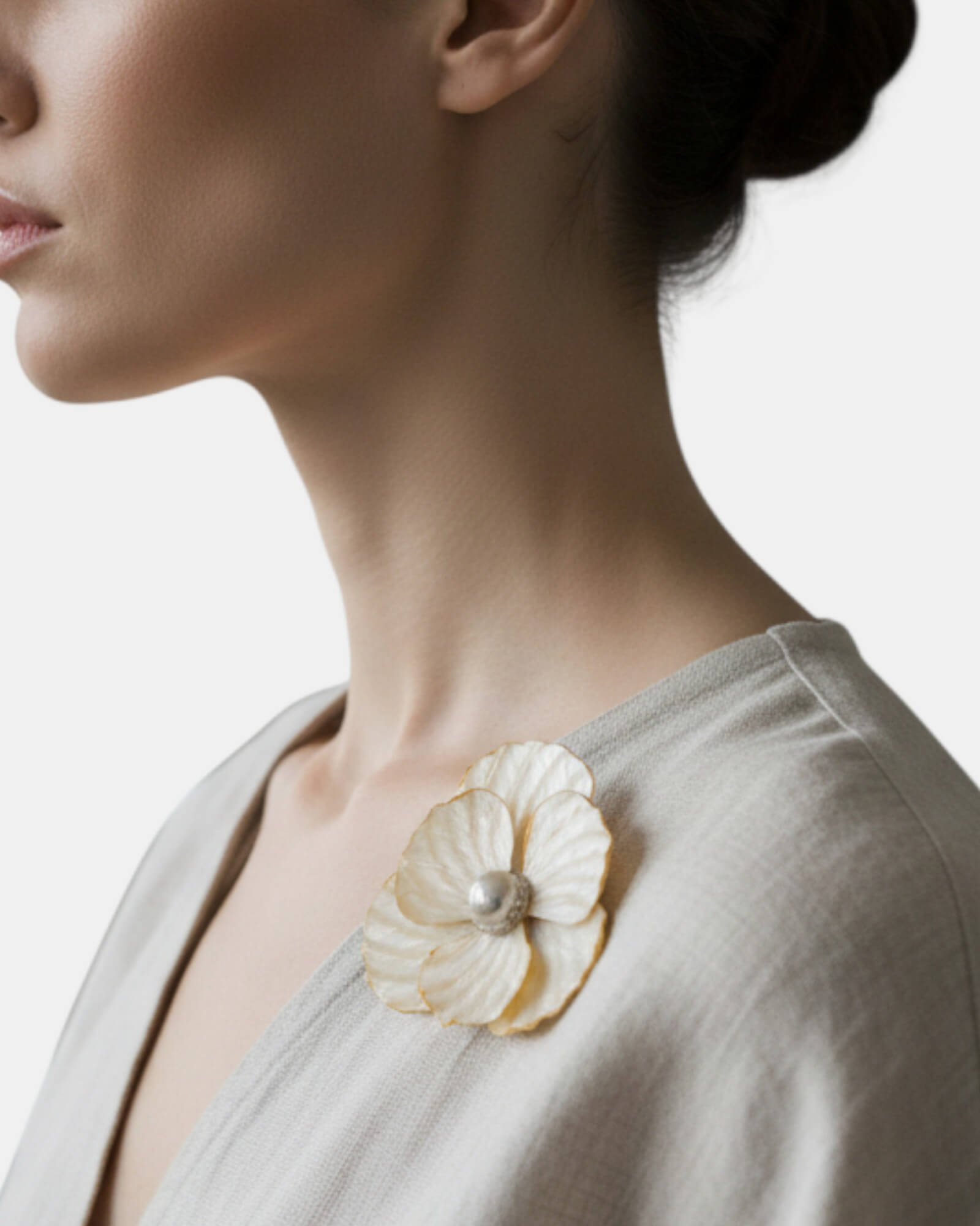 Broche de flor de nácar color marfil colocado sobre la solapa de un vestido de lino grisáceo en una modelo.