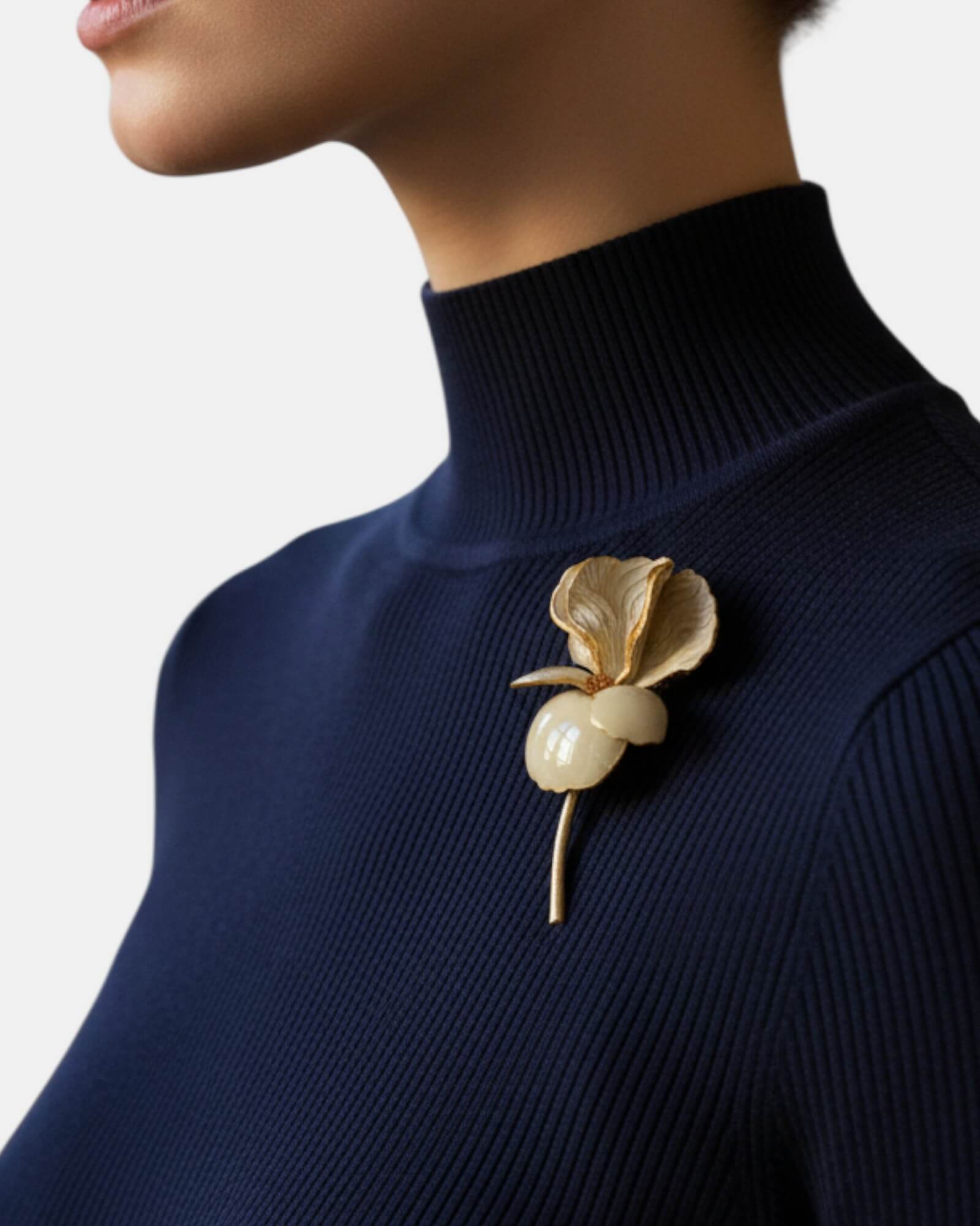 Mujer luciendo broche de flor beige sobre jersey de cuello alto azul marino, estilo minimalista y elegante.