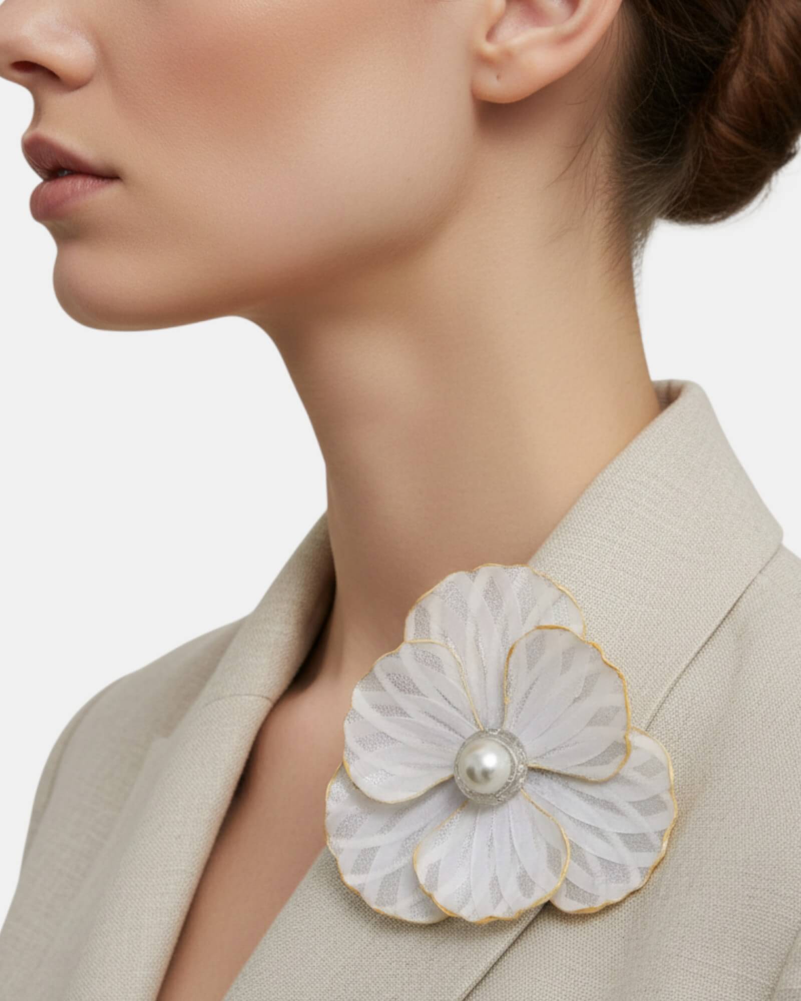 Broche grande de flor blanca con detalles plateados lucido en la solapa de una chaqueta blazer color beige.