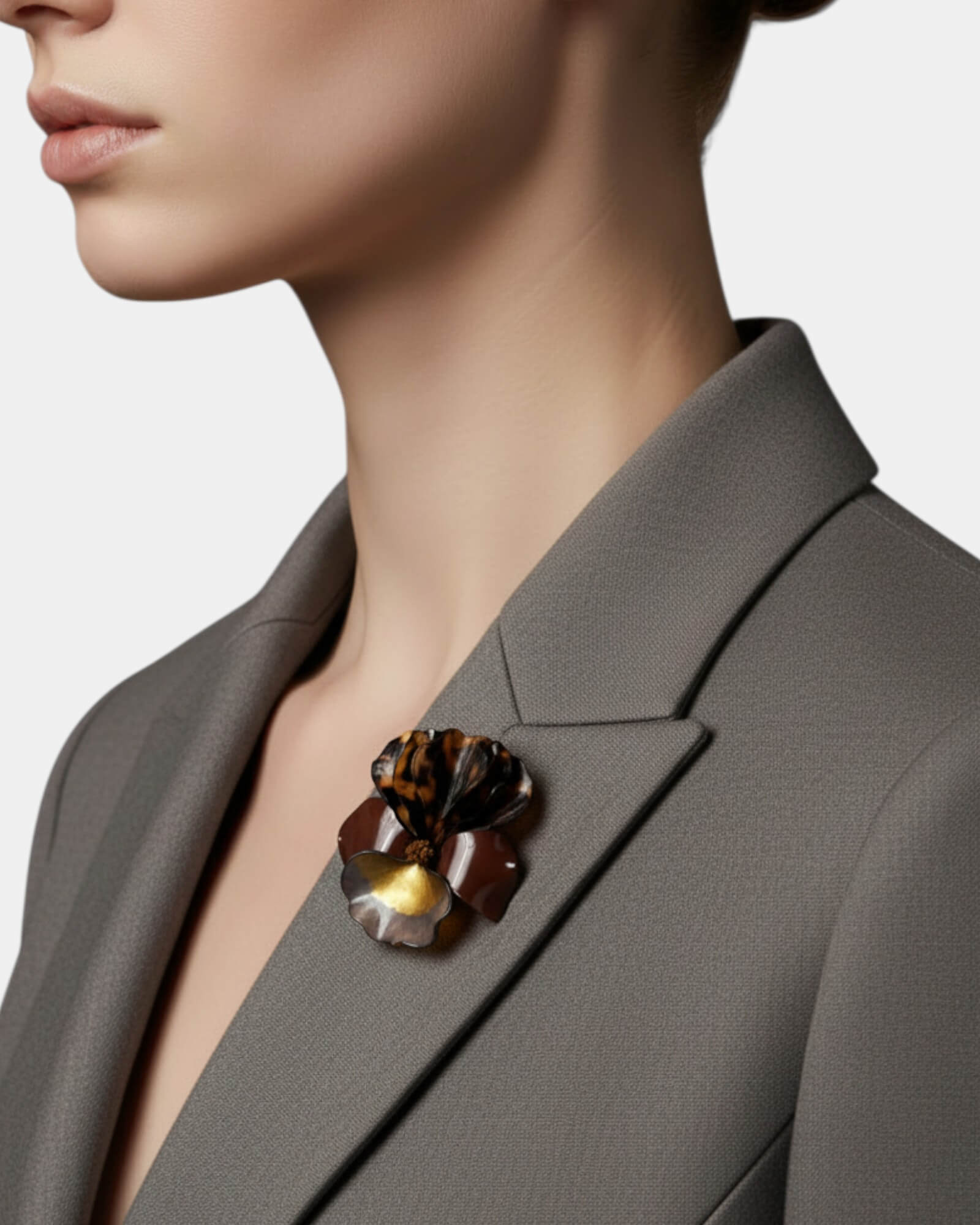 Broche escultórico con estampado carey y centro dorado metálico en solapa de blazer gris profesional."