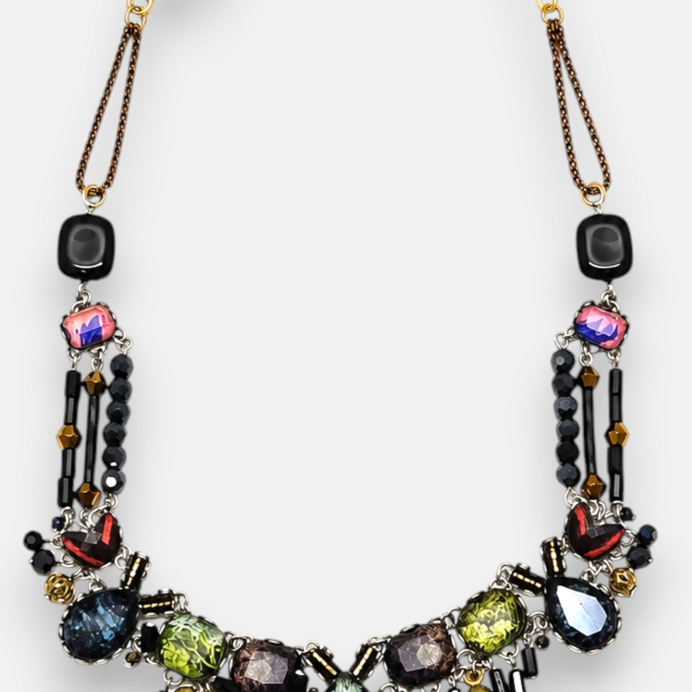diseño del collar dispuesto de forma arqueada sobre fondo neutro, destacando la composición en mosaico con tonos verdes, violetas y azules.