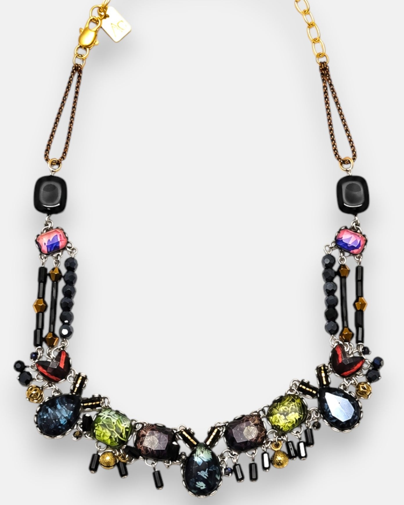 diseño del collar dispuesto de forma arqueada sobre fondo neutro, destacando la composición en mosaico con tonos verdes, violetas y azules.